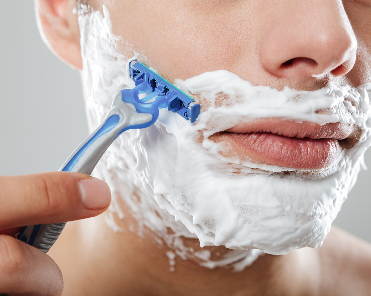 Detail na muža holiaceho sa žiletkou. Okolo úst má penu na holenie.